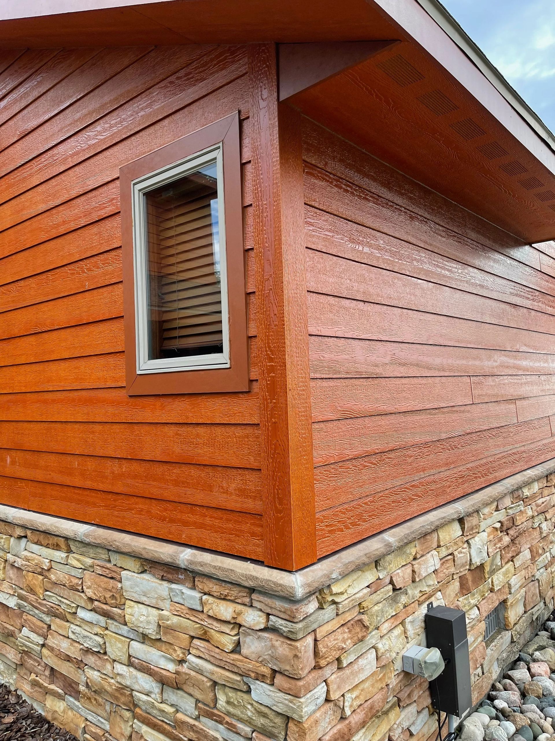 Orange textured house siding with a small window and stone base corner detail