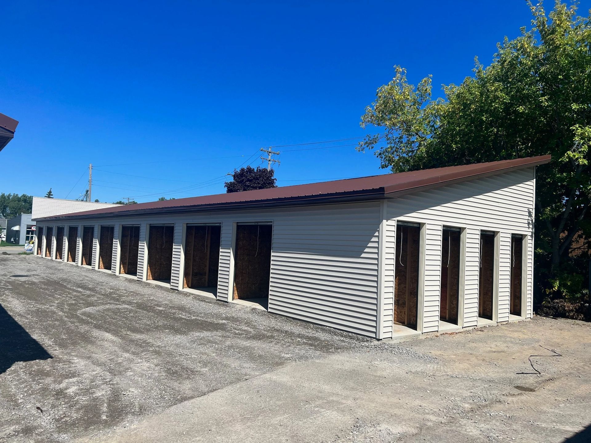 Long white brick building with many doors and a brown roof on a sunny gravel lot
