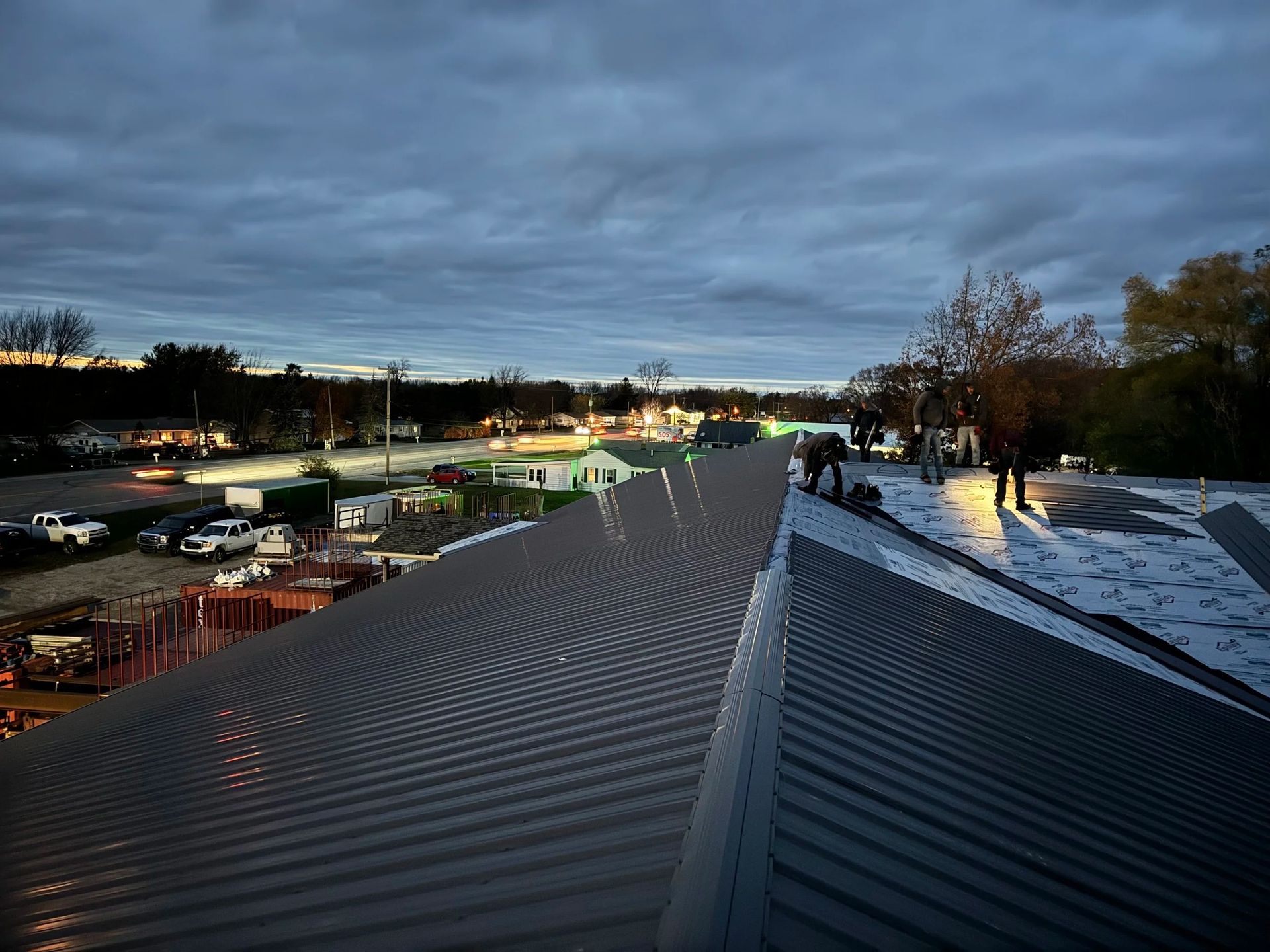 Rooftop with dark metal panels at dusk, overlooking a parking lot and cloudy sky