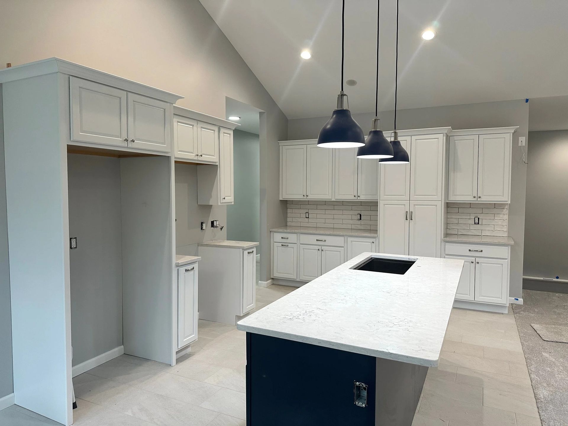 Modern white kitchen with island and pendant lights, featuring cabinets and a built-in refrigerator.