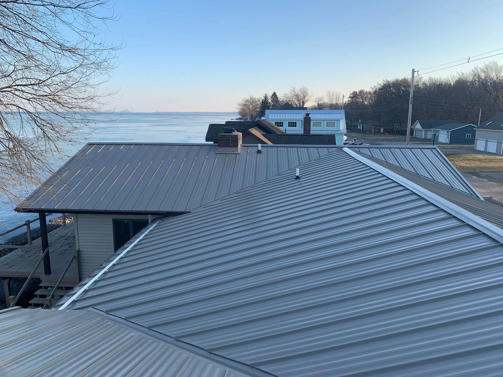 Snow-covered metal roof beside a frozen lake under a clear blue sky