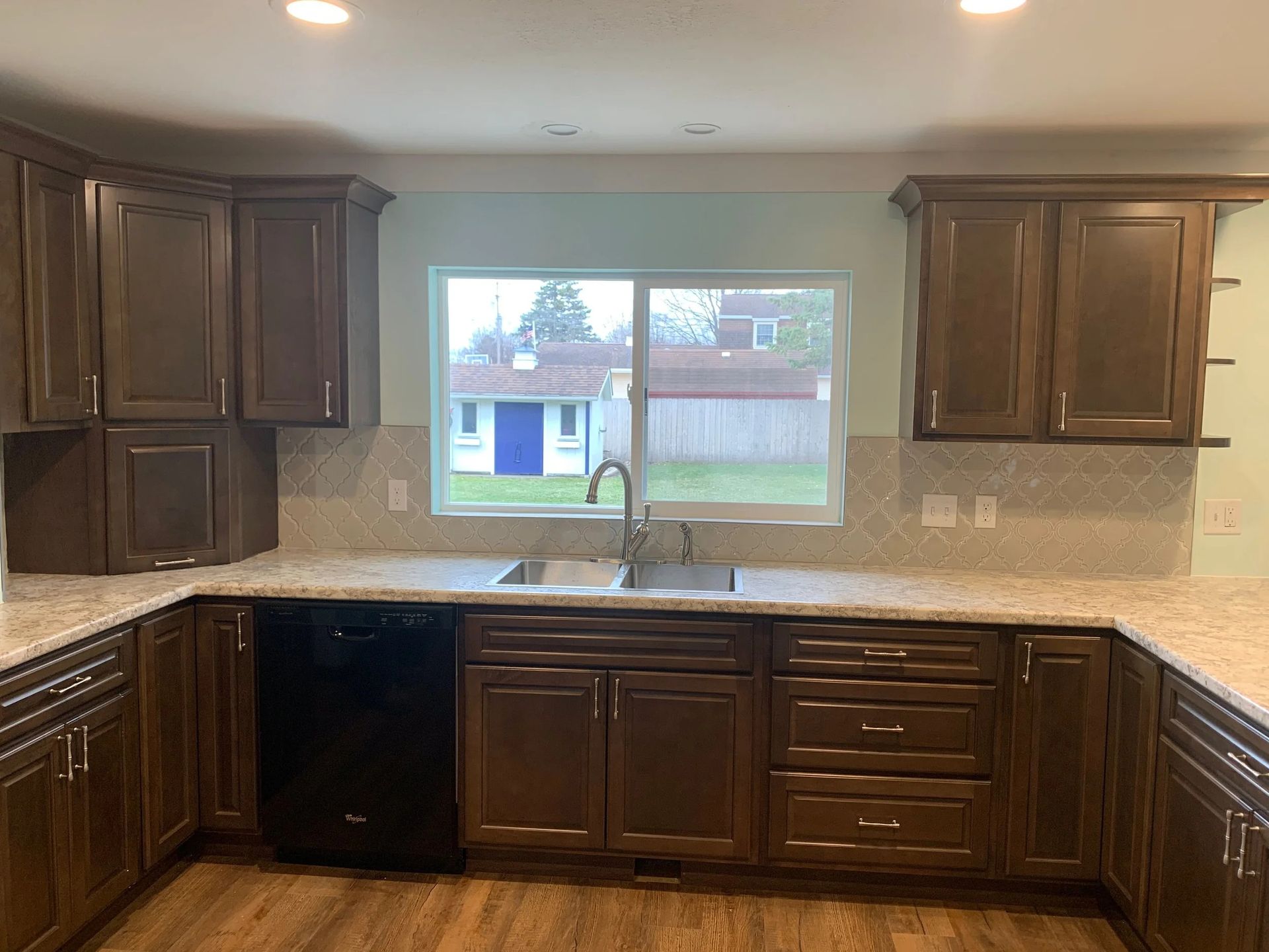 Empty kitchen with dark wood cabinets, granite countertops, and a window over the sink.