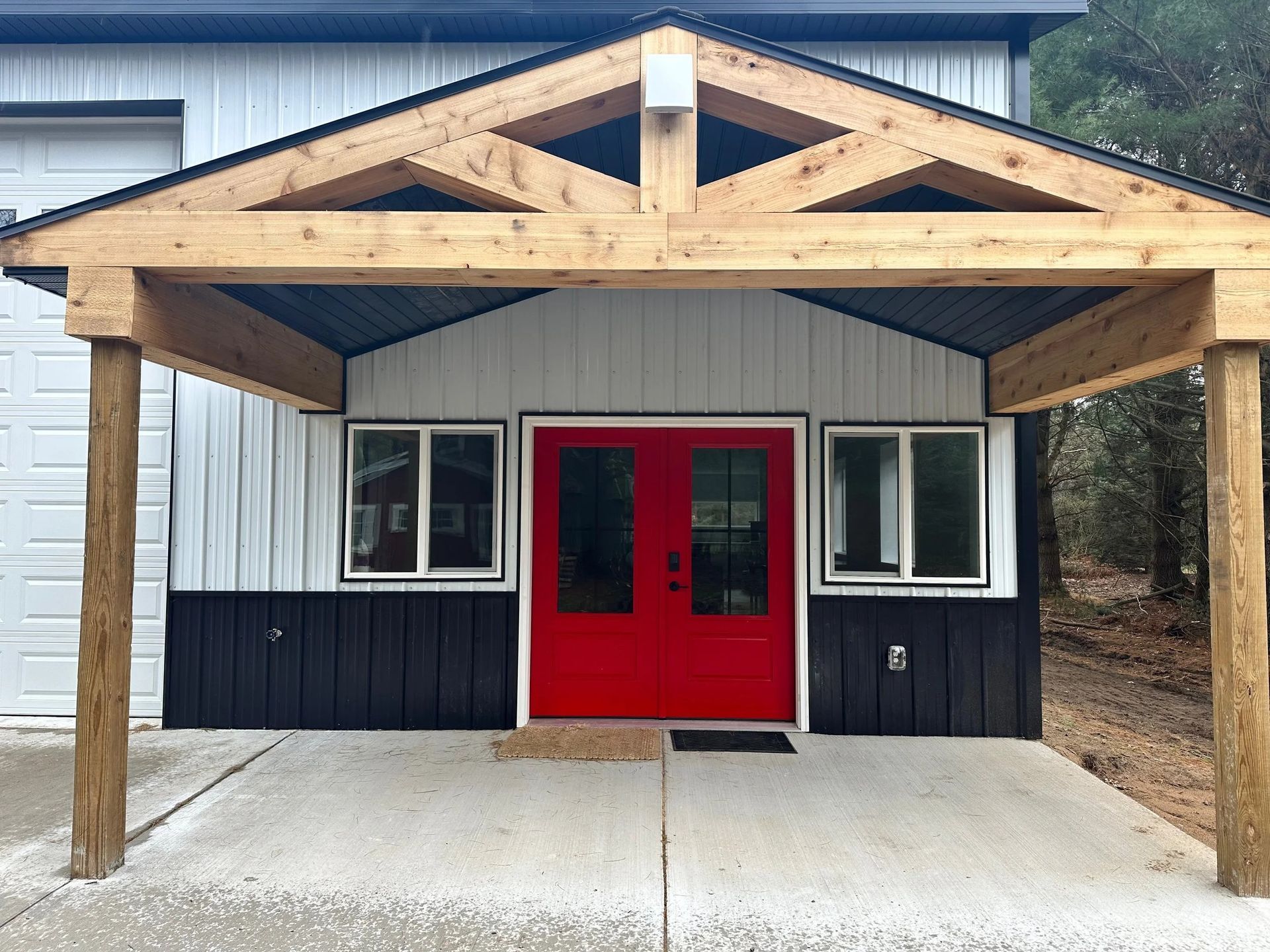 Small building entrance with red double doors, white siding, dark trim, and a wooden porch roof.