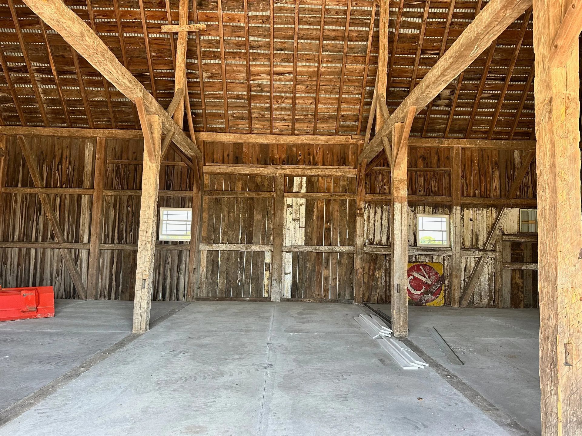 Open wooden barn interior with support beams, dirt floor, and a red crate on the left.