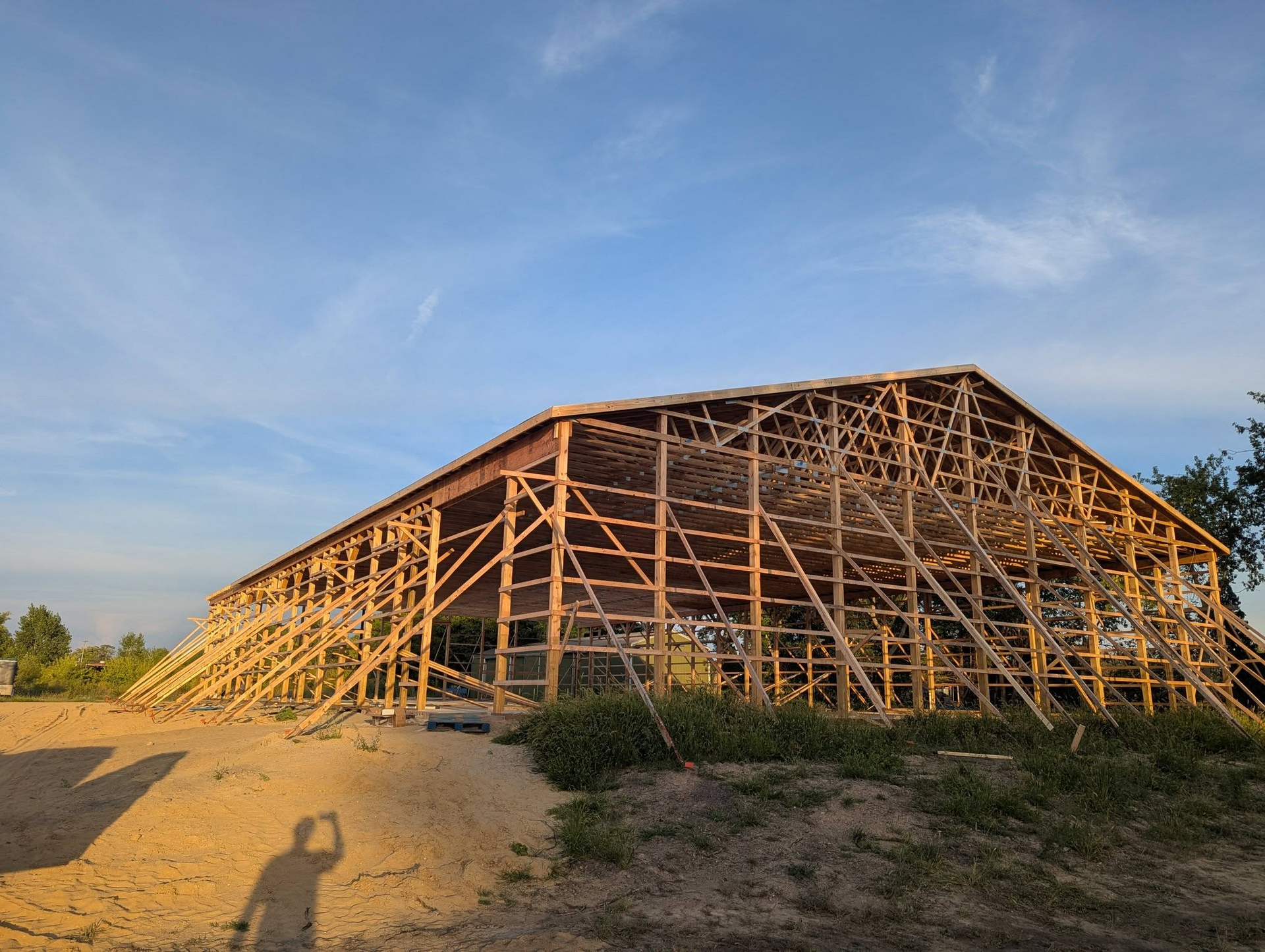 Wooden barn frame under construction on a sandy lot at sunset
