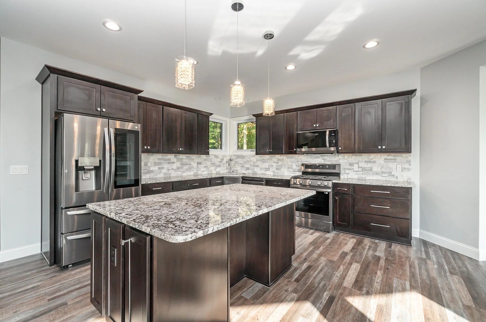 Modern kitchen with dark cabinets, stainless steel appliances, large island, and pendant lights