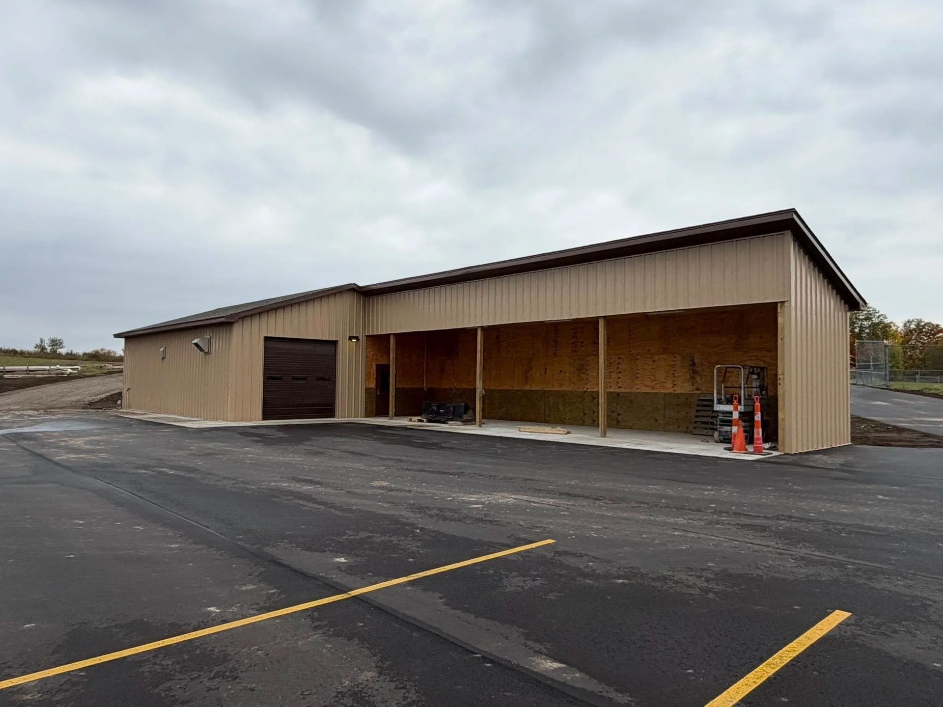 Partially built tan metal warehouse with open front and parked equipment in an empty lot