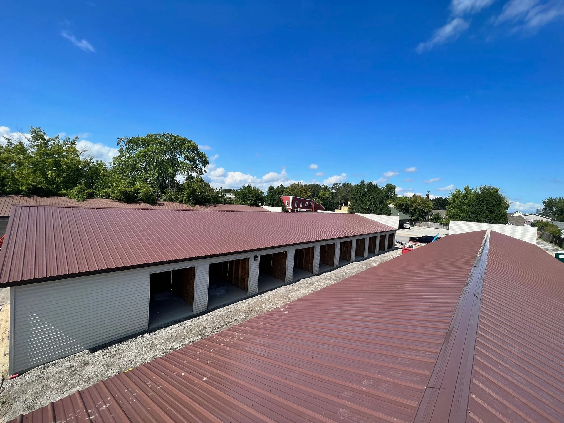 Long red-roofed building under a bright blue sky, viewed from above with trees in the background