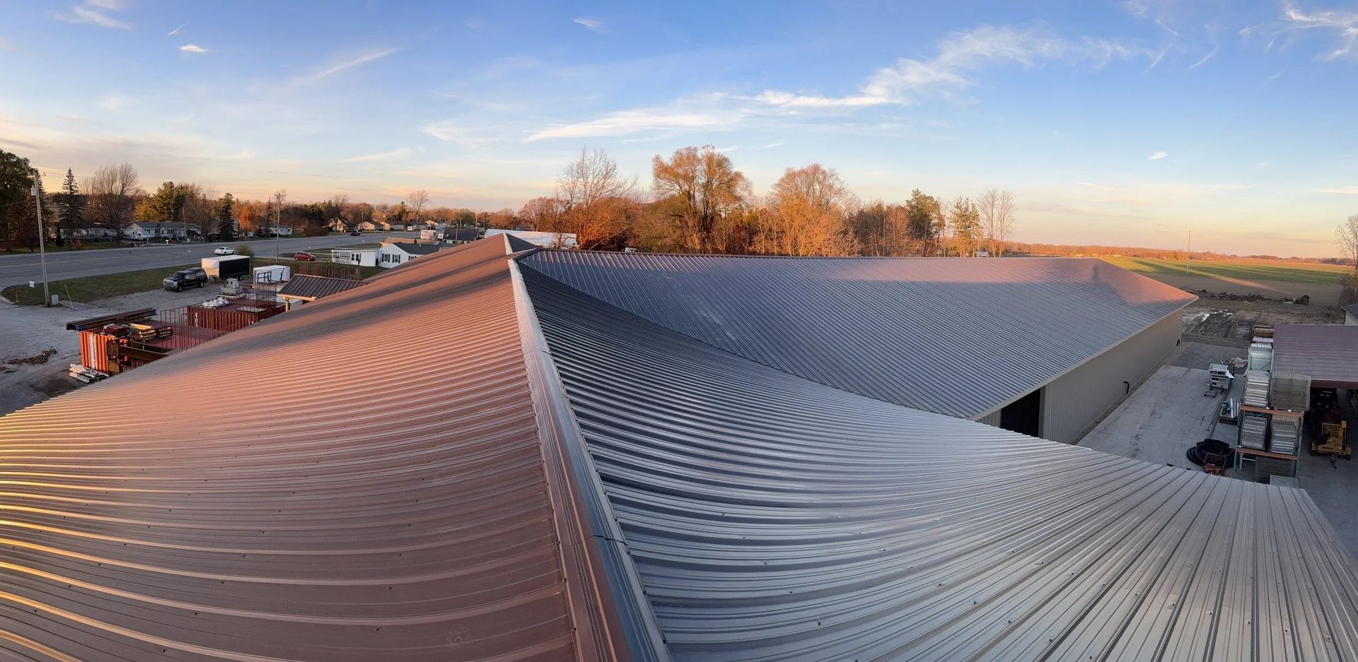 Rooftop with wavy white metal panels at sunset, overlooking parked cars and autumn trees