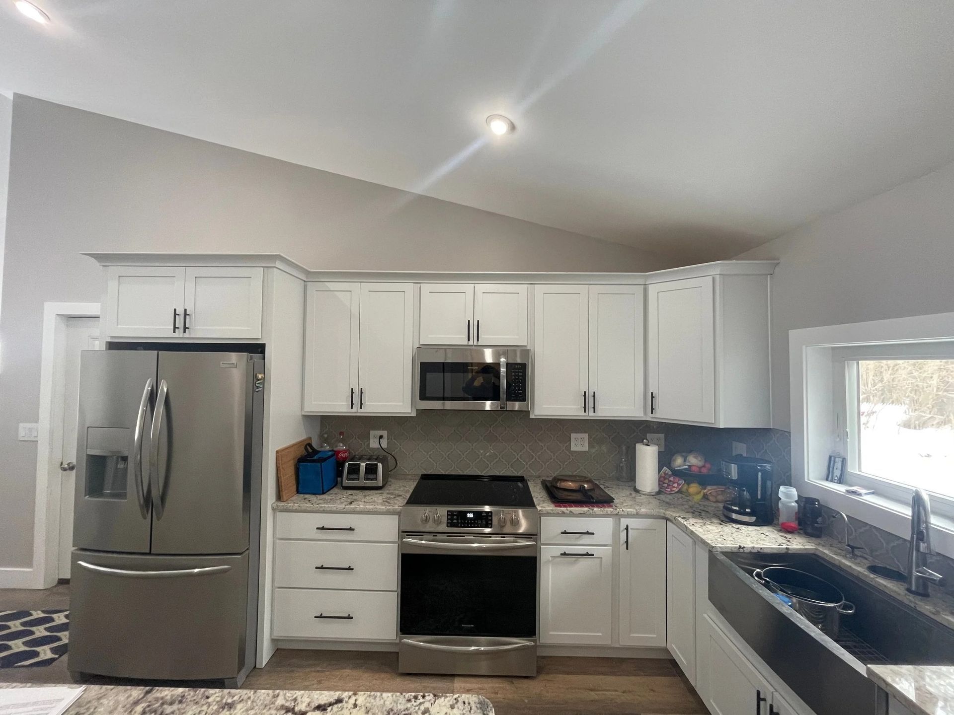 Bright white kitchen with stainless steel appliances, white cabinets, and a large window over the sink.