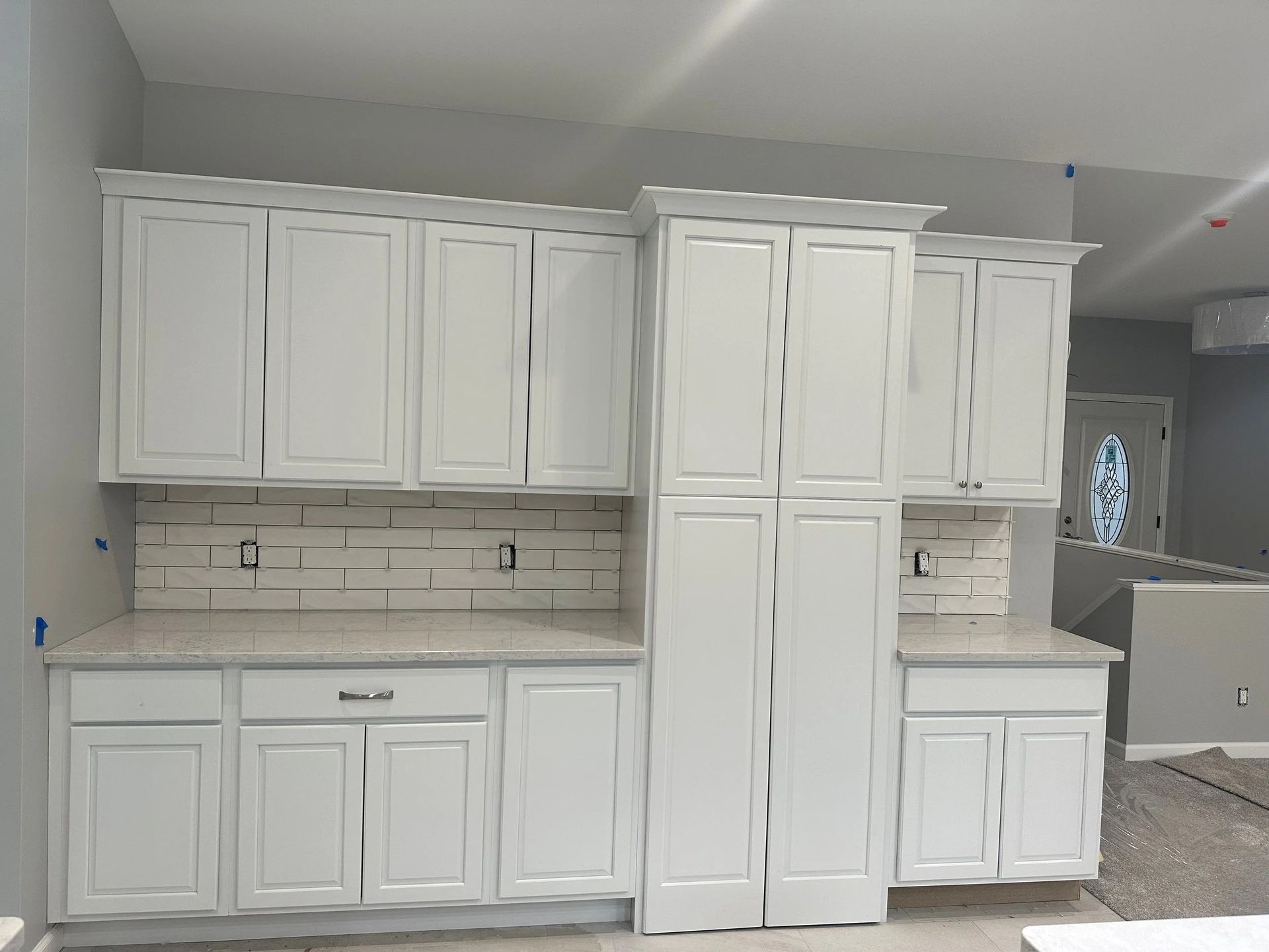 White kitchen cabinets and island installed in a bright, unfinished kitchen with tiled backsplash
