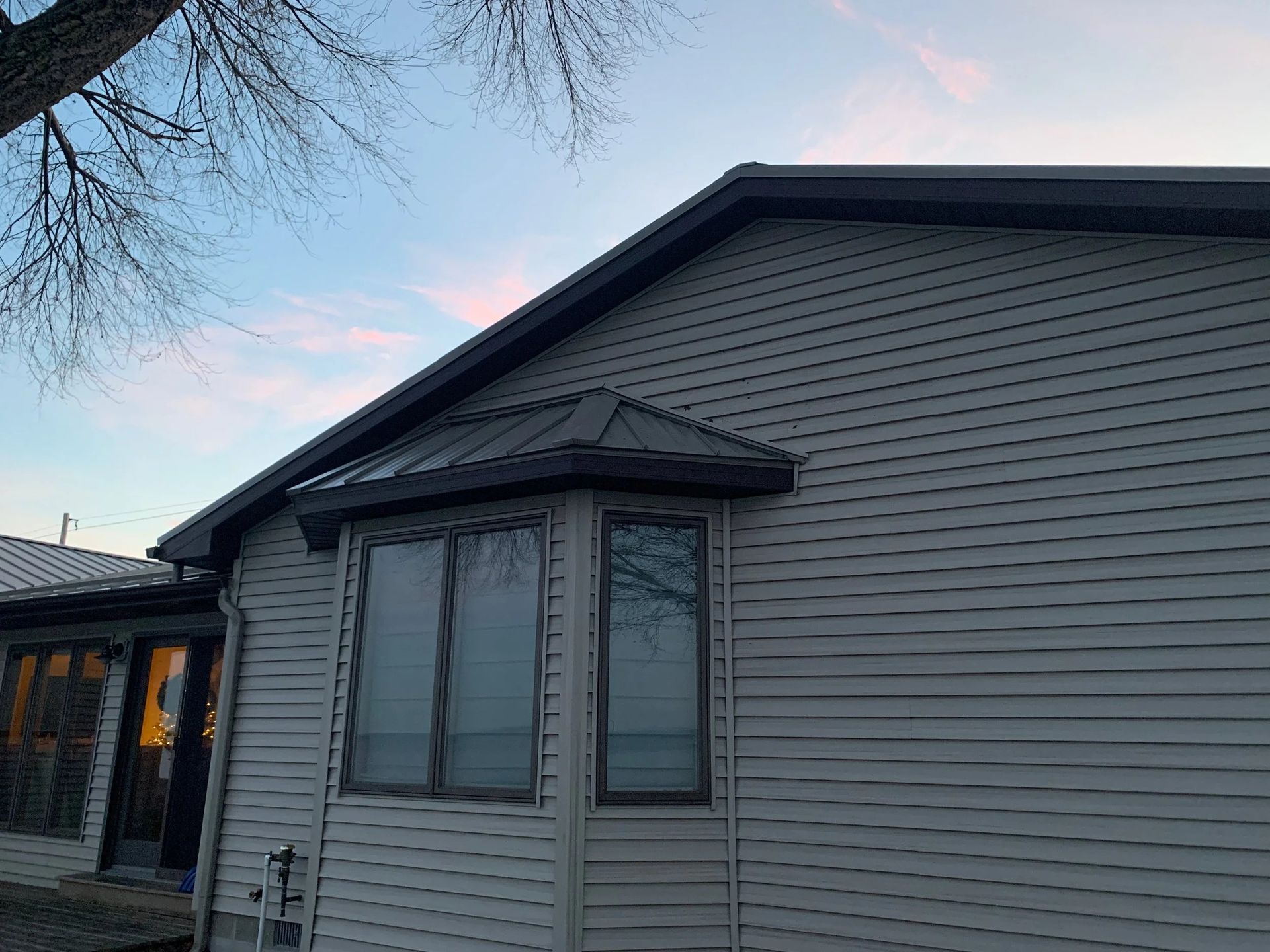 Exterior of a gray house with a bay window and dark roof at dusk