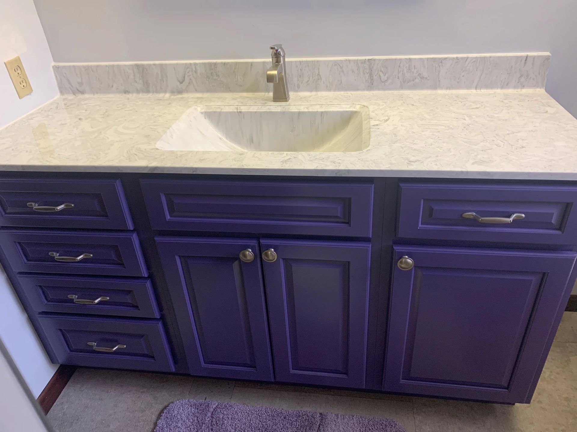 Purple bathroom vanity with white countertop, built-in sink, and chrome faucet