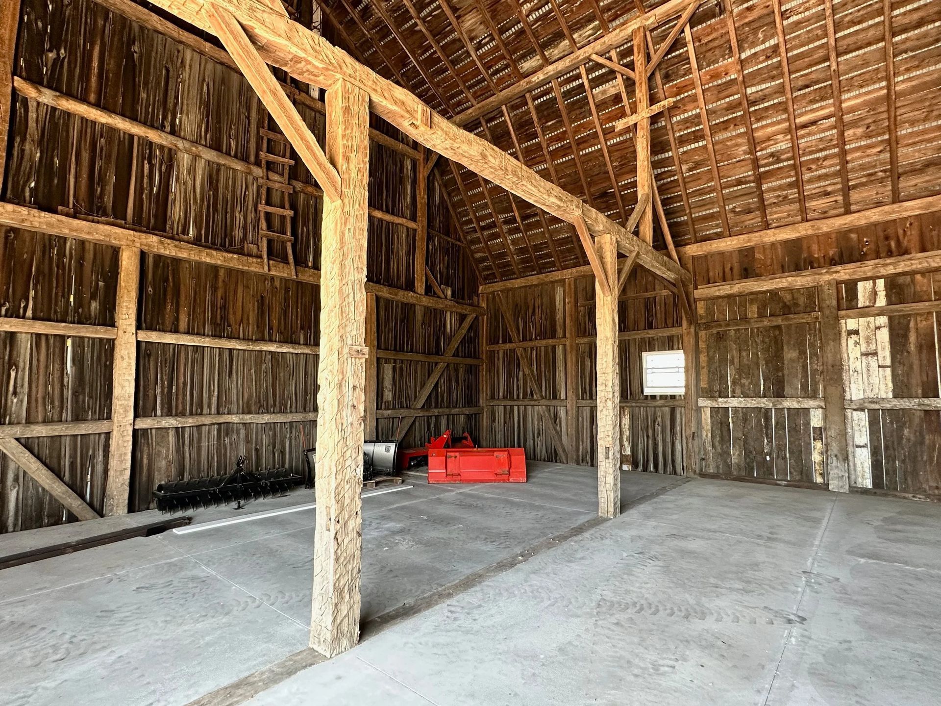 Empty rustic barn interior with wooden beams, dirt floor, and a red tool chest against the far wall