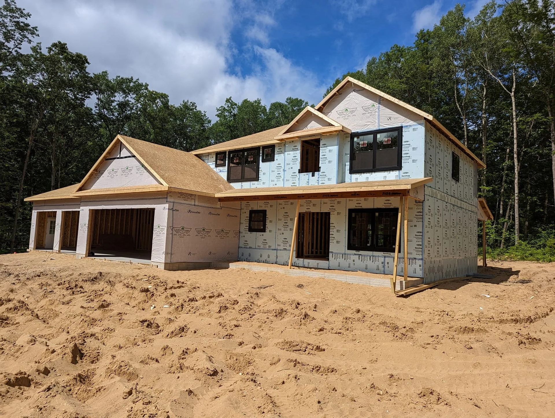 Partially built two-story house with stone exterior and garage on sandy lot under blue sky