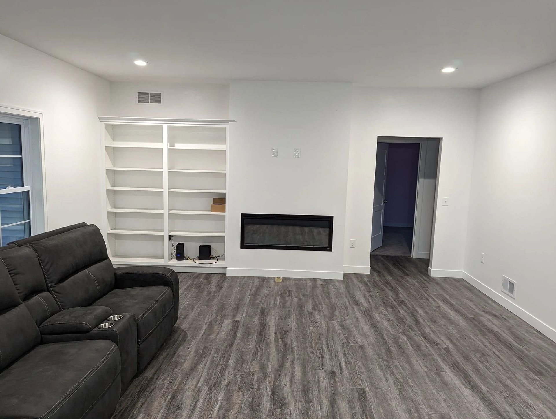 Empty living room with white built-in shelves, black sofa, gray carpet, and a wall fireplace