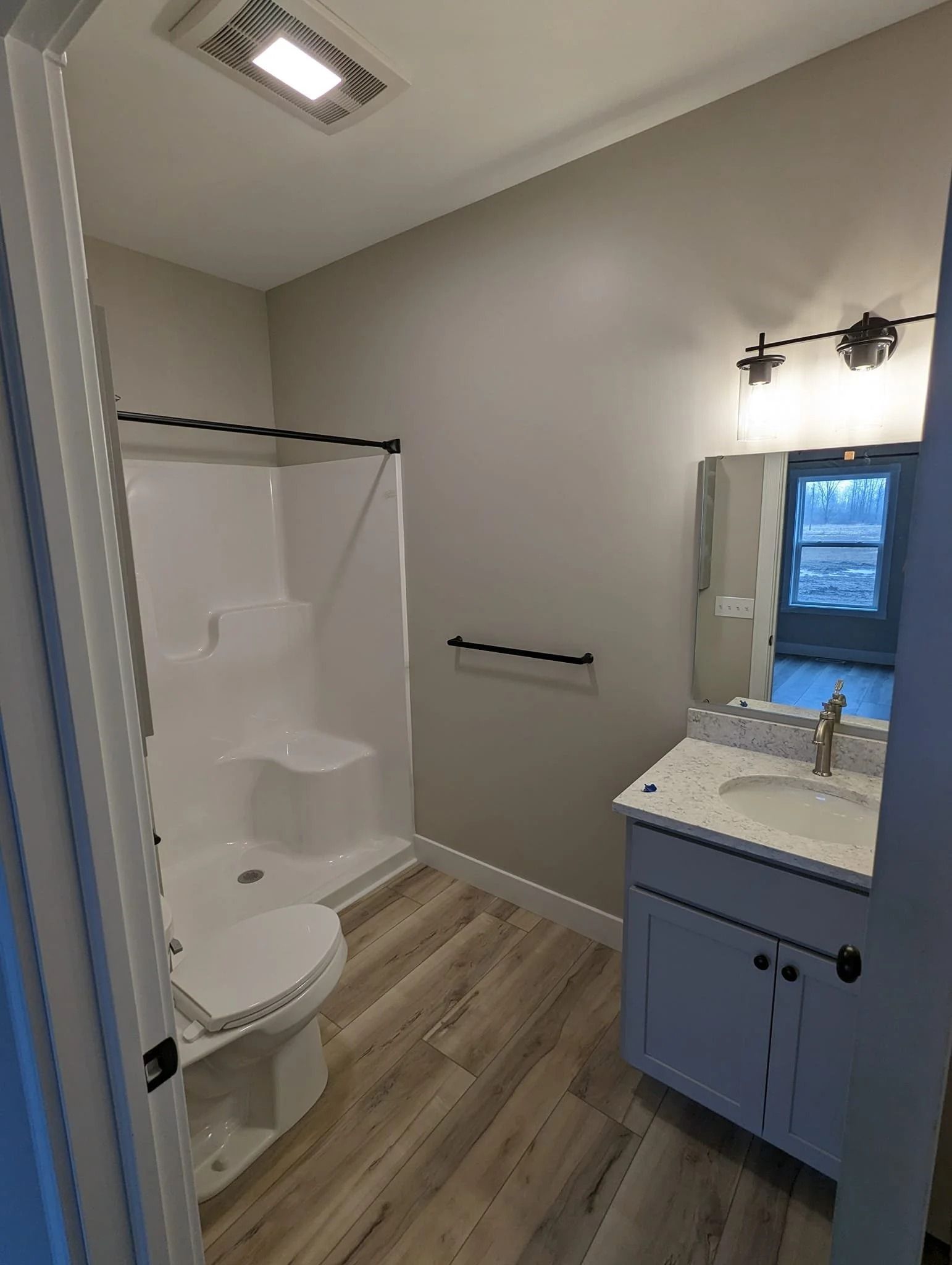 Small bathroom with walk-in shower, toilet, vanity, and window with blue cabinet accents.