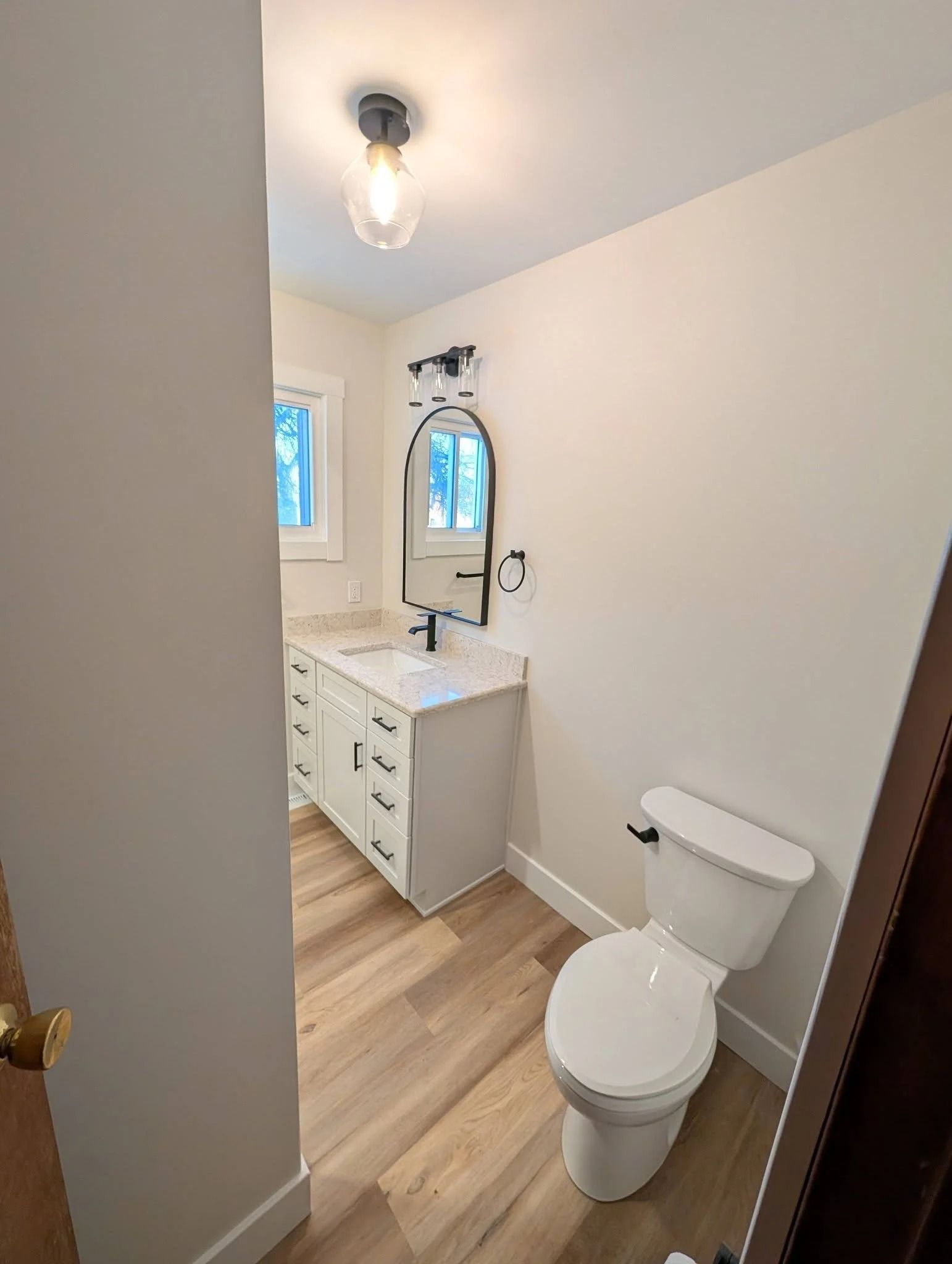 Small white bathroom with a vanity, toilet, window, and wood-look floor.
