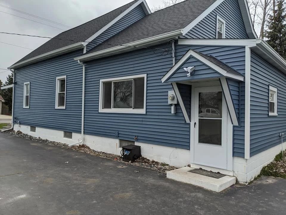 Blue house exterior with white trim, covered porch, and driveway on a cloudy day