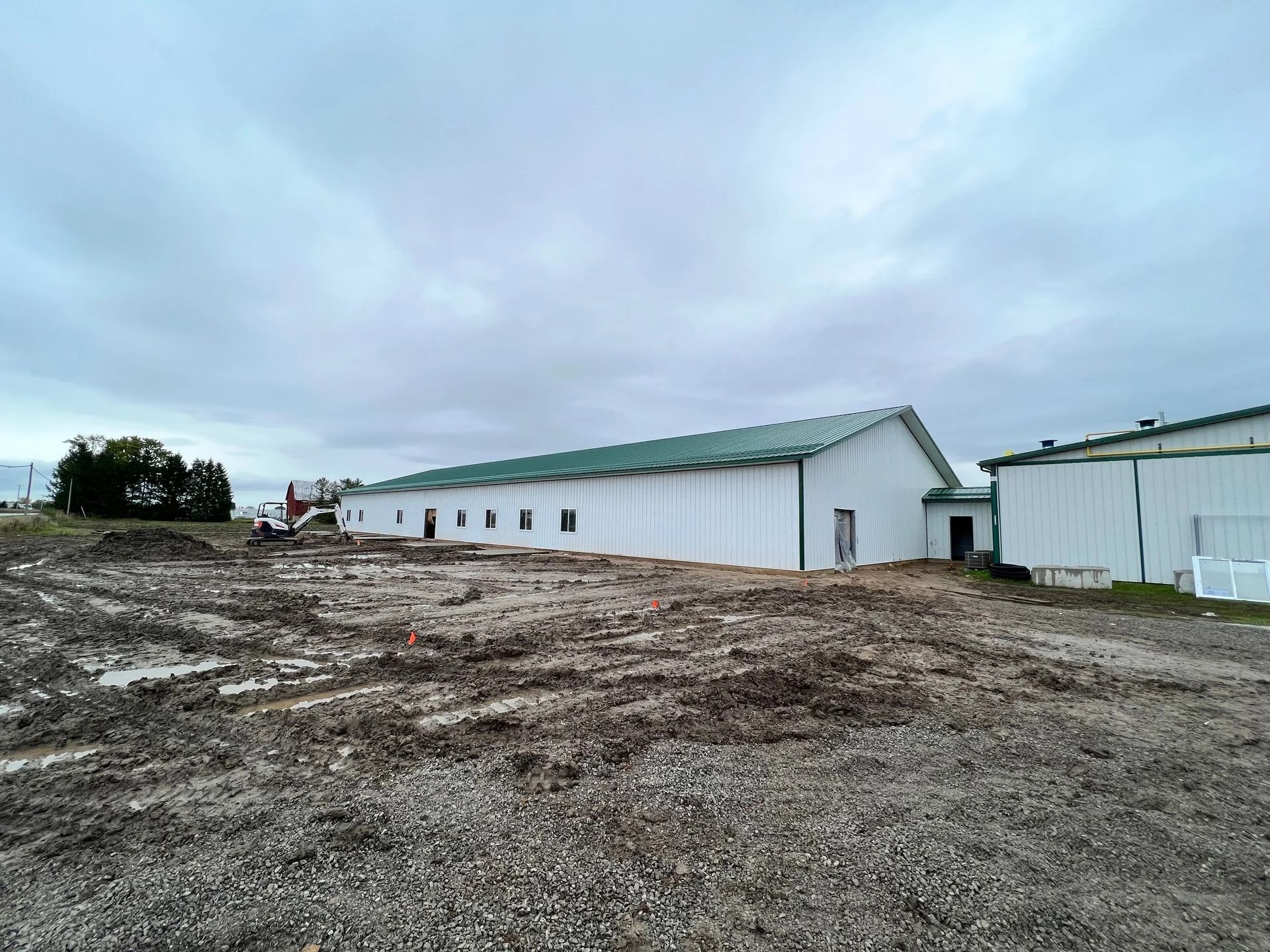 Long white industrial building on a muddy lot under a cloudy sky