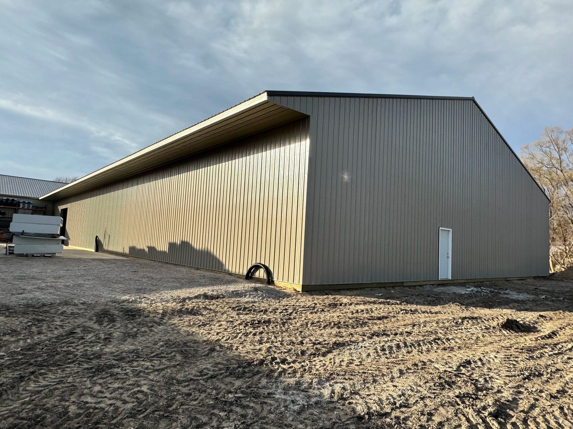 Long tan barn-like building with striped siding on a gravel lot under a blue sky