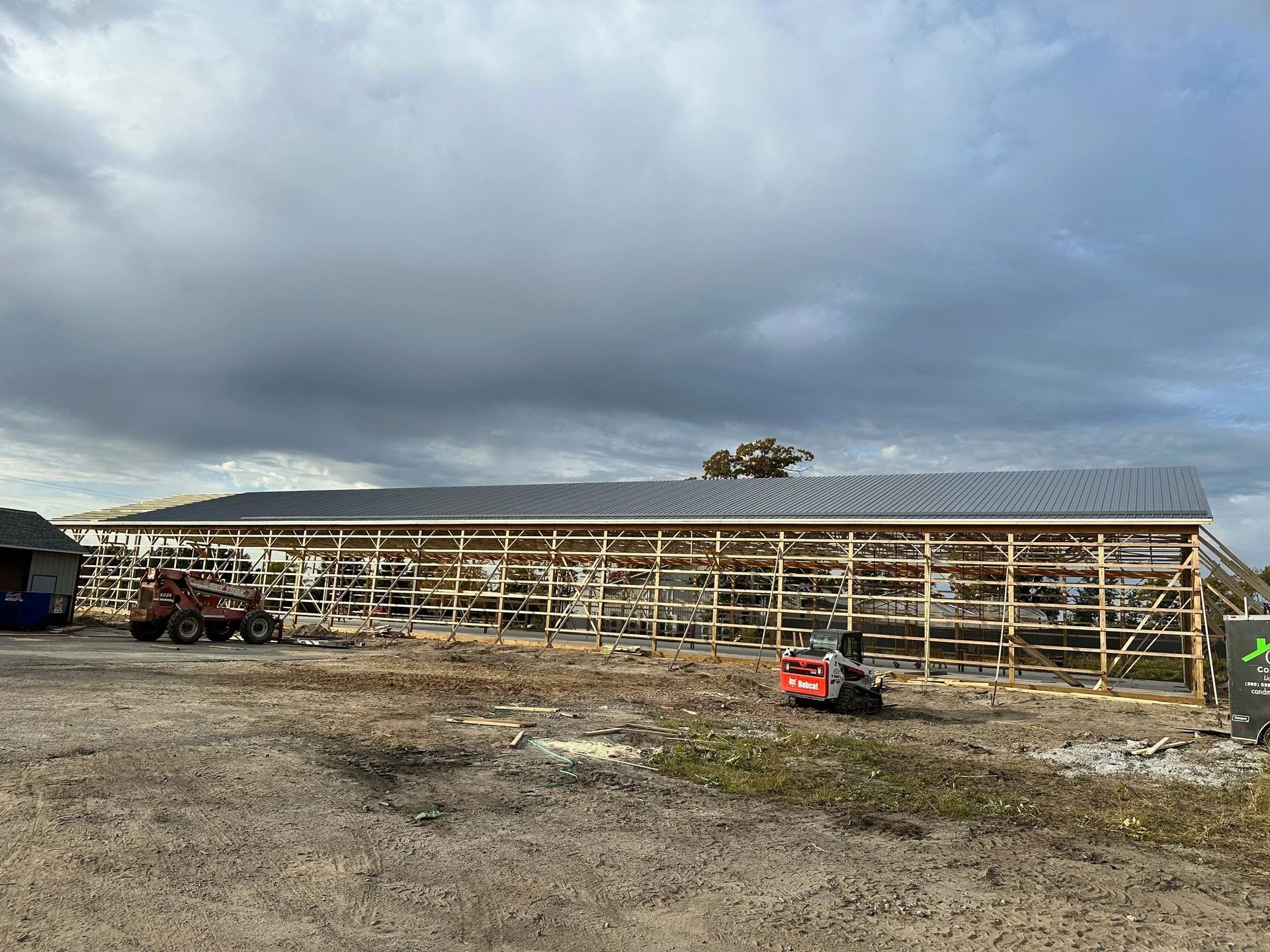 Long row of greenhouse frames under a cloudy sky on a muddy farm site