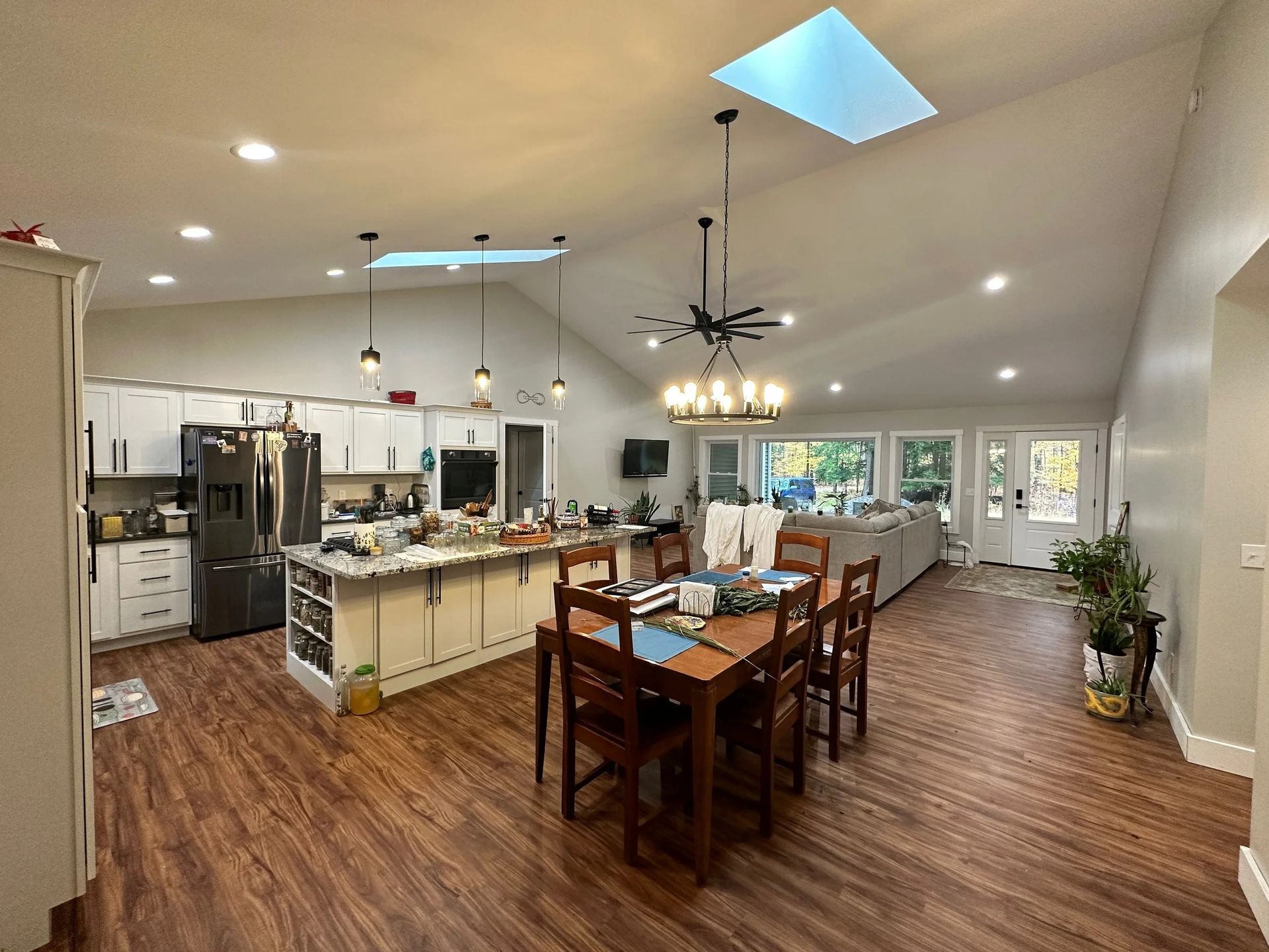 Open kitchen and dining area with wood floors, island seating, chandelier, and skylight in a bright home interior