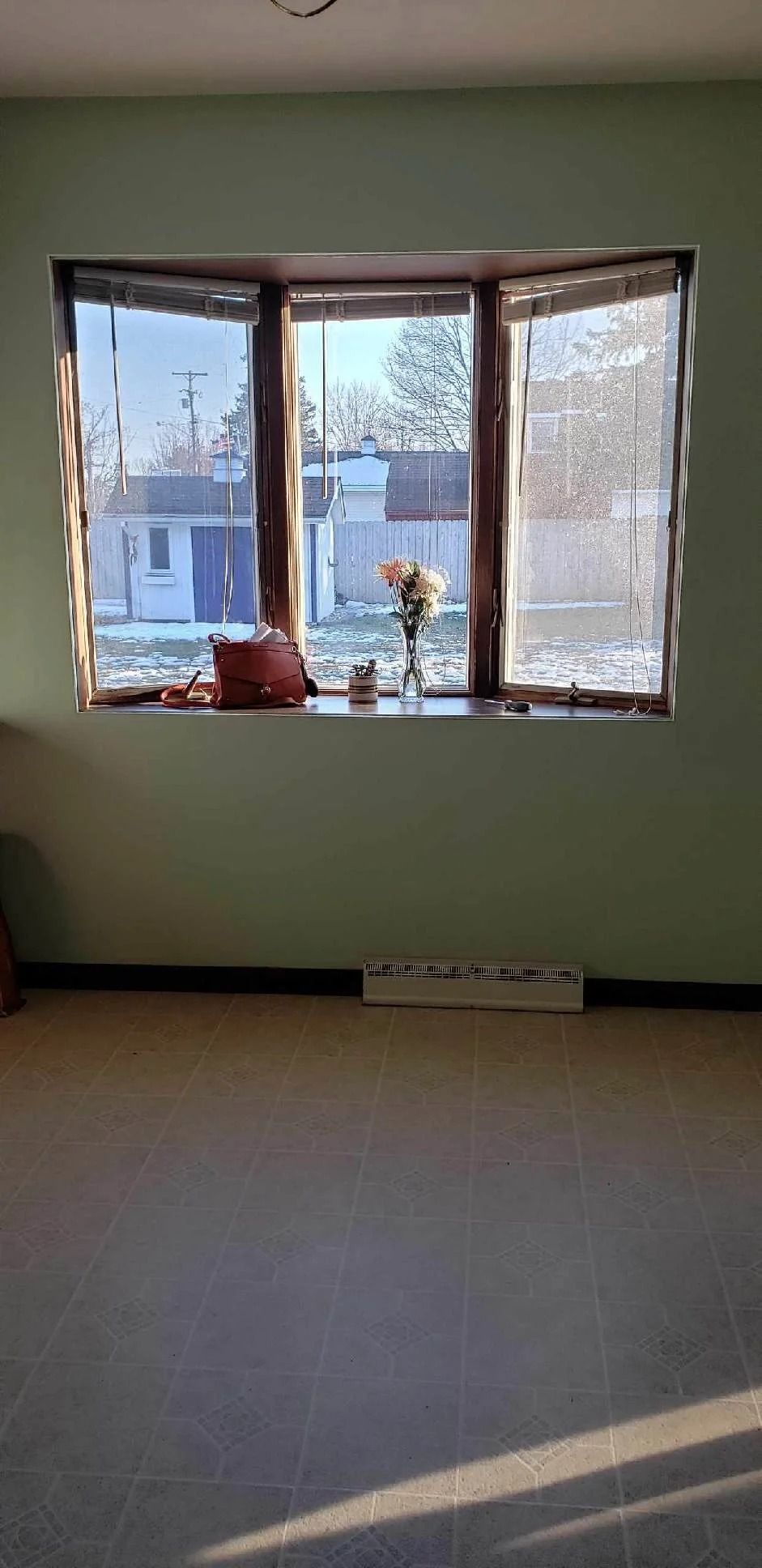 Empty room with a large bay window, pale green walls, and sunlight on the floor