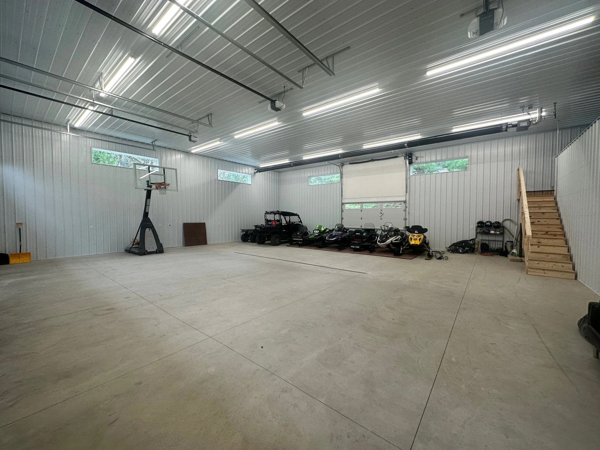 Large empty indoor warehouse with concrete floor, metal walls, bright strip lights, and equipment stored along one side