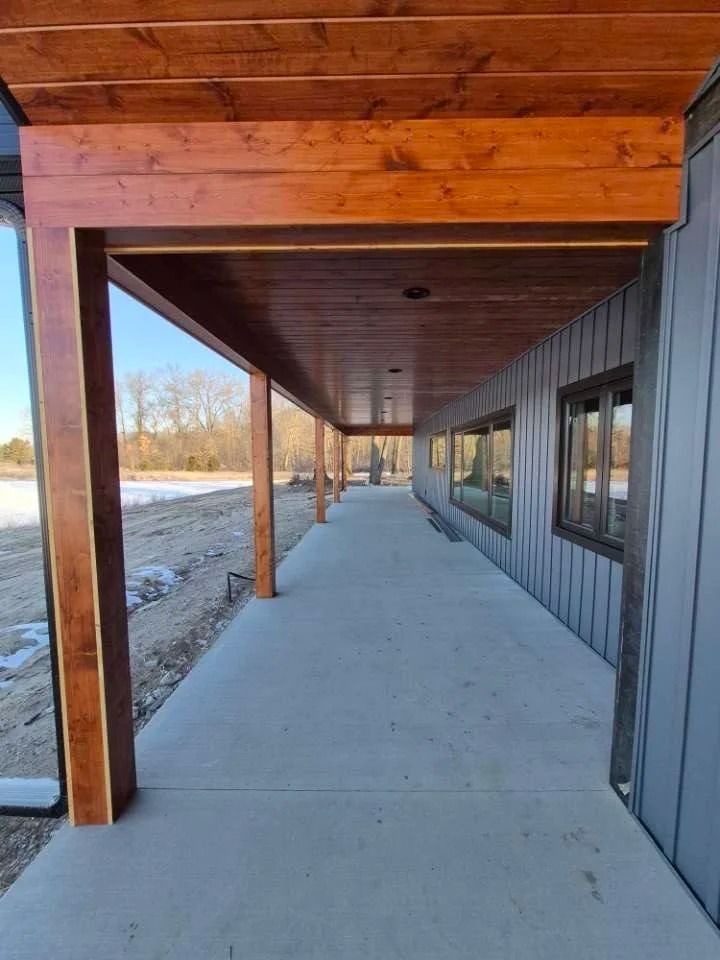 Covered concrete walkway beside a building, with wooden beams and windows along the right side.
