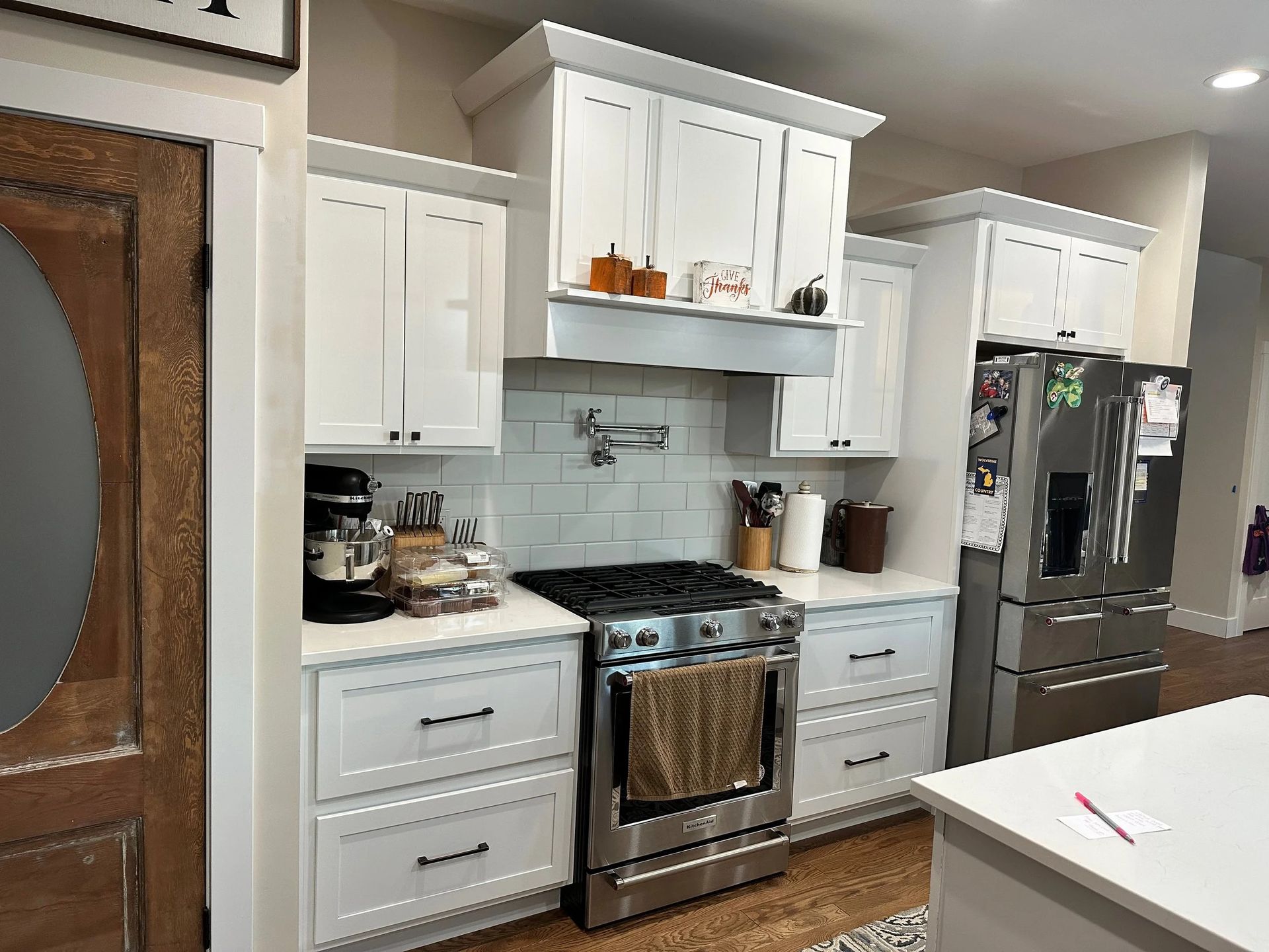 Modern white kitchen with stainless steel appliances, black countertops, and a kitchen island edge in the foreground
