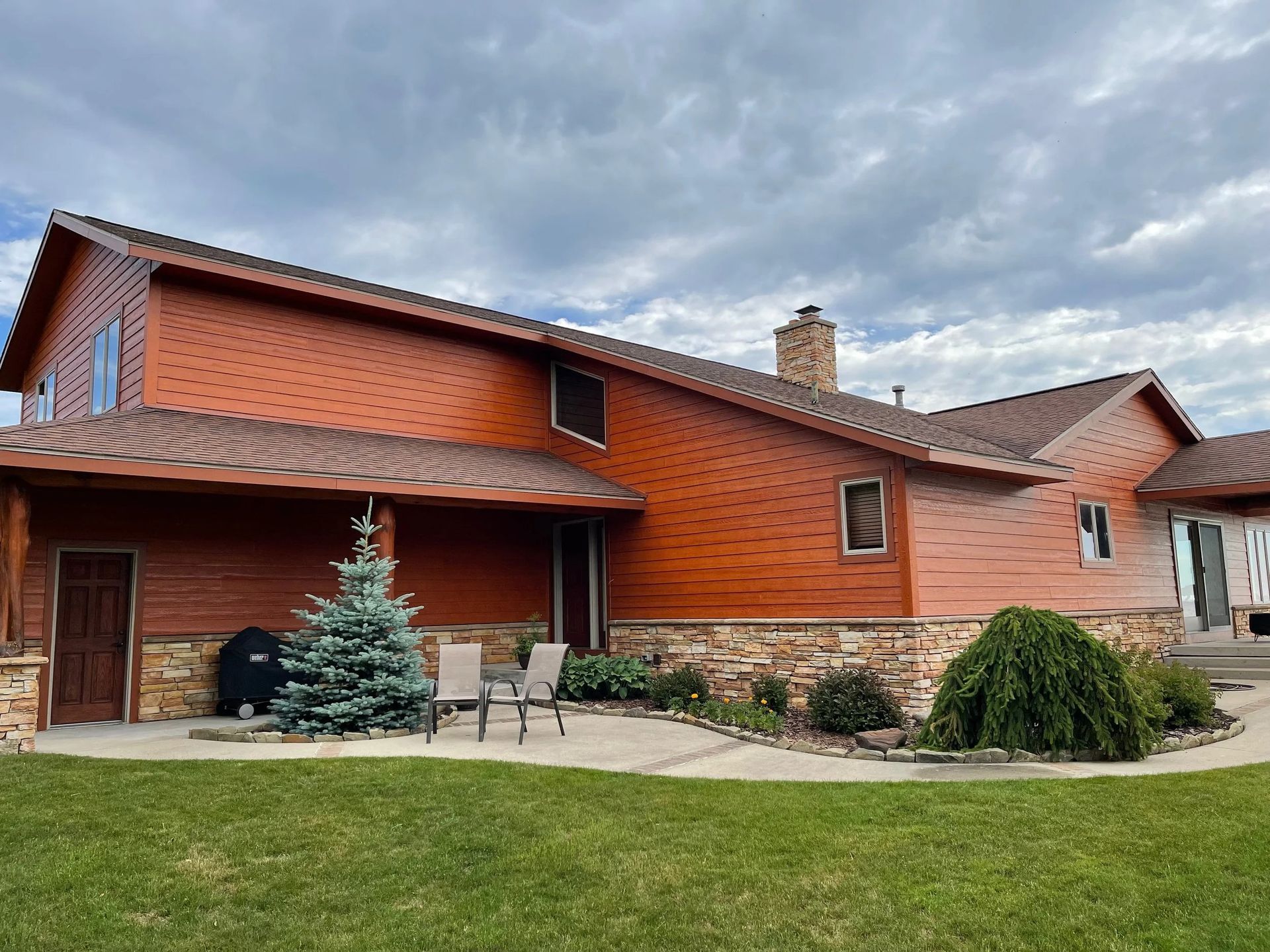 Two-story brick and wood house with a covered patio and landscaped front yard under cloudy skies