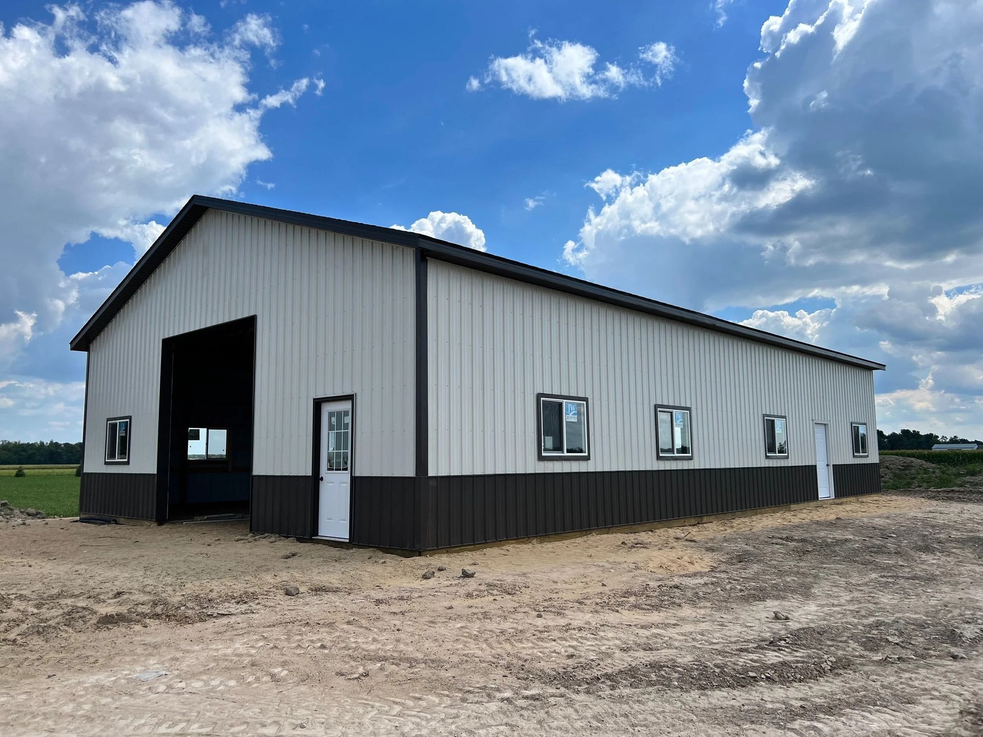 White metal barn or workshop with black trim on a gravel lot under a blue, partly cloudy sky.
