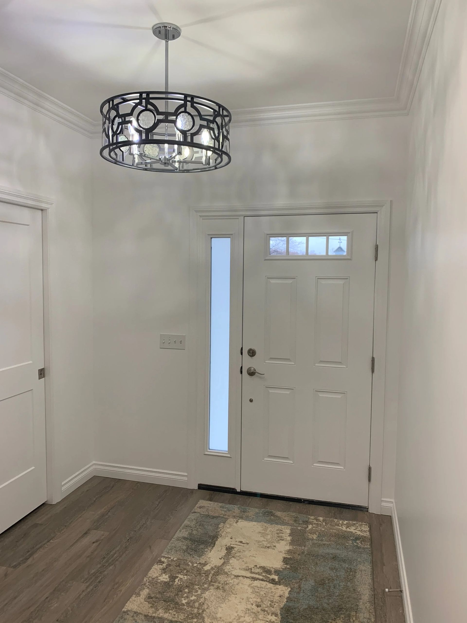 Bright entryway with white front door, pendant light, hardwood floor, and a patterned rug