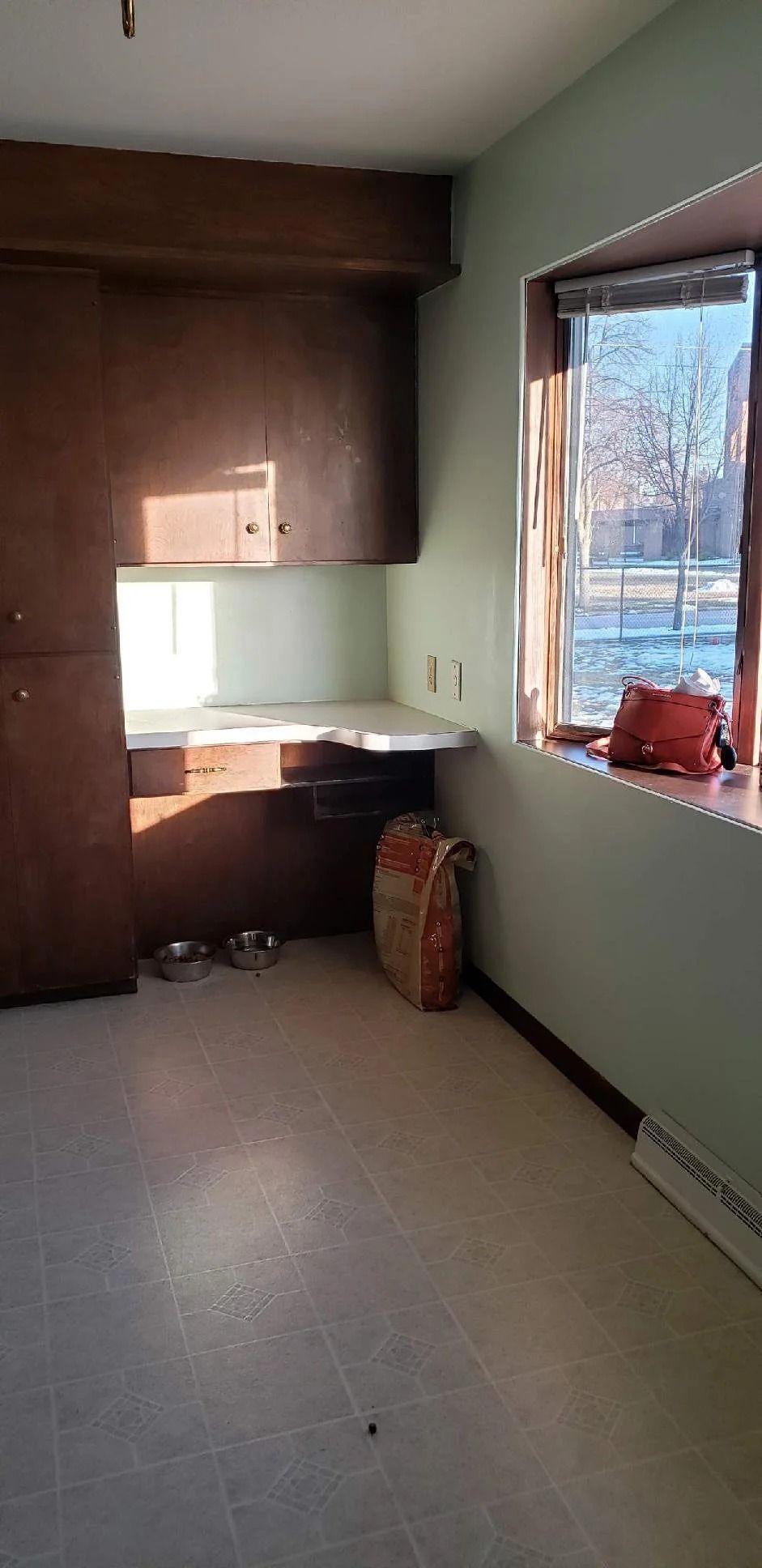 Empty room with built-in wooden desk, pale green walls, and sunlight through a window