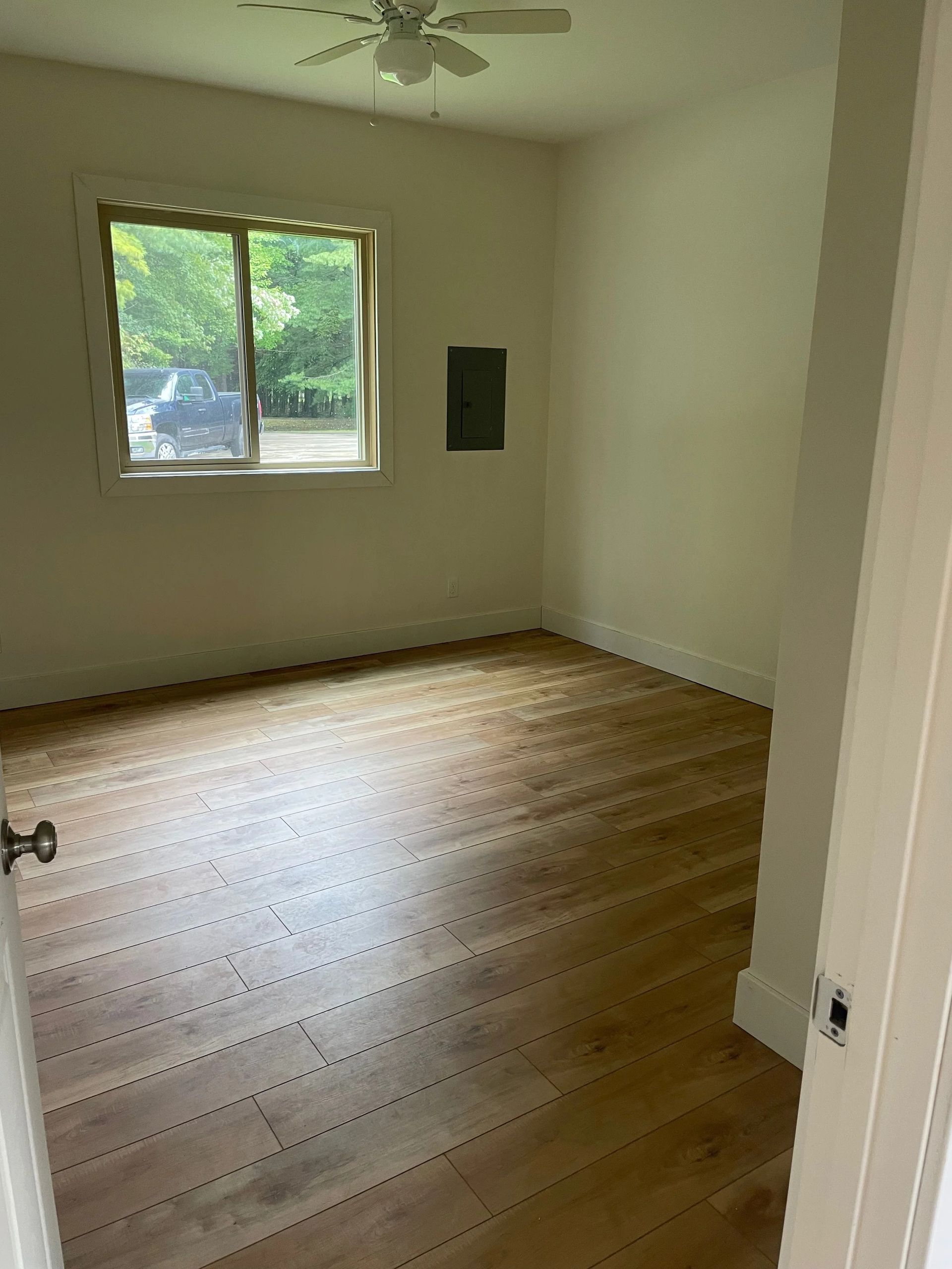 Empty room with hardwood floor, white walls, window, and ceiling fan.