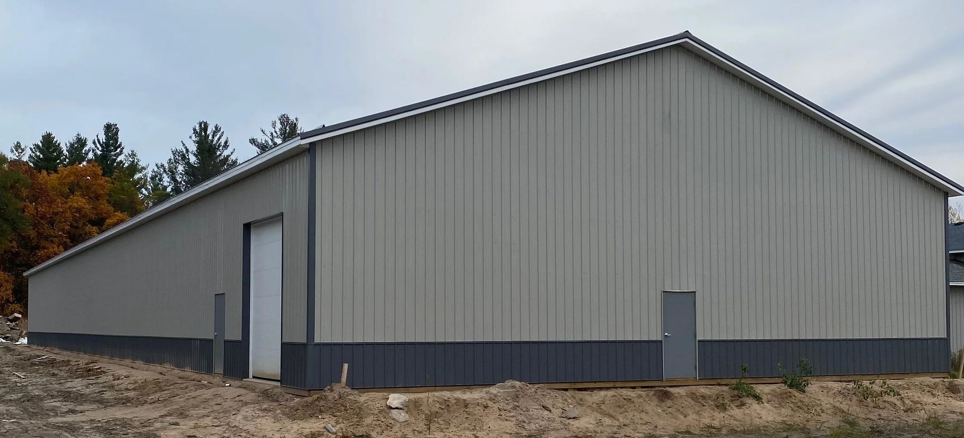 Large gray metal barn with a gabled roof on a dirt lot