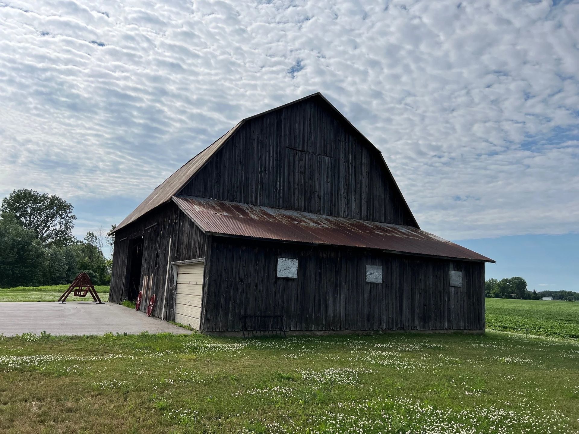Old weathered barn with a red metal roof in a grassy field under a cloudy sky