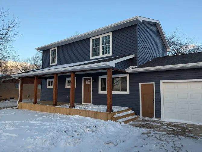 Snow-covered two-story house with dark siding, white trim, and a garage in front