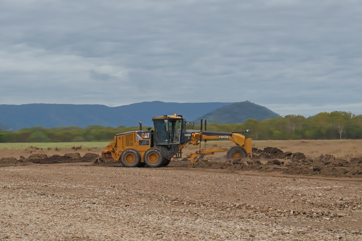 A Yellow Tractor is Plowing a Dirt Field With Mountains in the Background — Advanced Civil Earthworks In Mount Isa, QLD