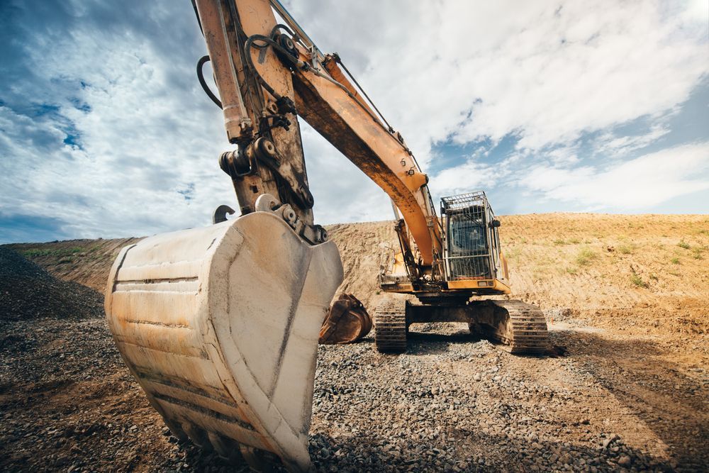 A Large Excavator is Digging a Hole in a Dirt Field — Advanced Civil Earthworks In Cassowary Coast, QLD