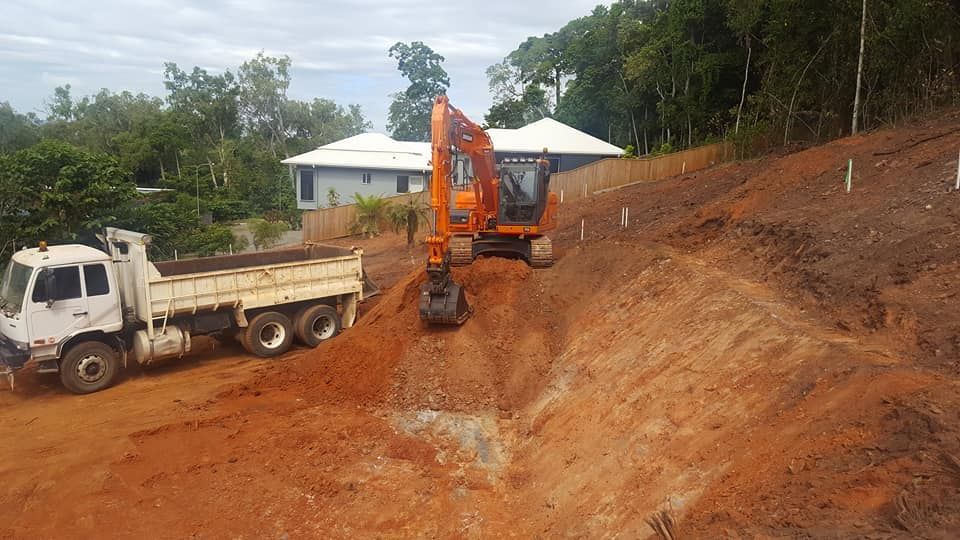A Dump Truck is Driving Down a Dirt Road Next to an Excavator — Advanced Civil Earthworks In Koah, QLD