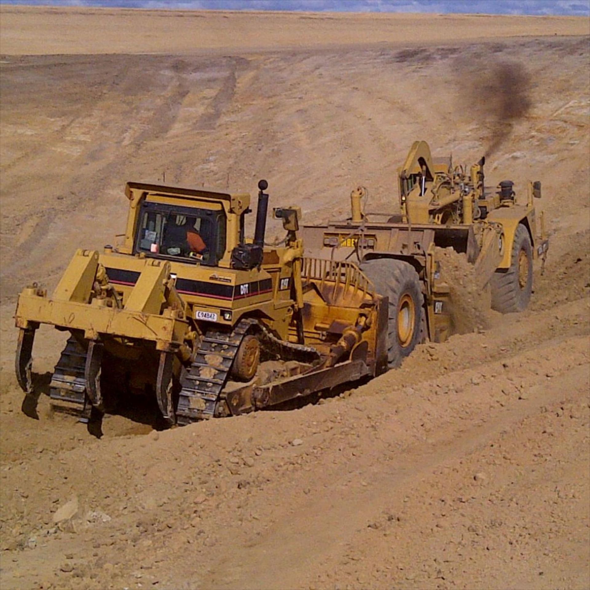 A Bulldozer Pulling Another Bulldozer on a Dirt Road — Advanced Civil Earthworks In Innisfail, QLD
