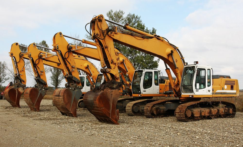 A Row of Yellow Excavators Are Parked in a Gravel Lot — Advanced Civil Earthworks In Innisfail, QLD