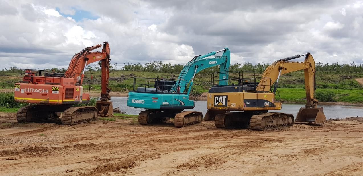 Three Excavators Are Parked Next to Each Other in a Dirt Field — Advanced Civil Earthworks In Cairns, QLD