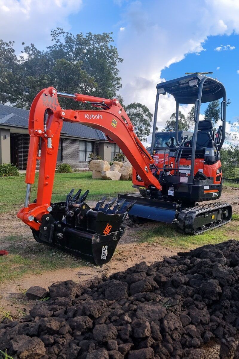 A Small Excavator is Sitting on Top of a Pile of Dirt in Front of a House — Advanced Civil Earthworks In Kuranda, QLD