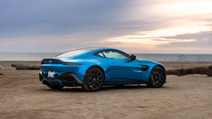 Blue sports car parked on a dirt road by the coast at sunset