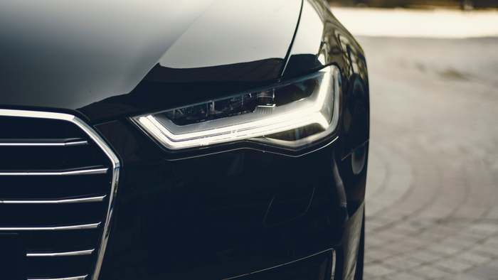 Close-up of a black car’s front grille and LED headlight on a paved surface.
