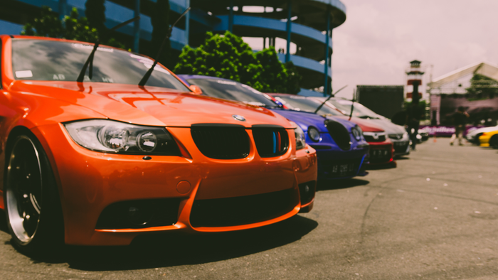 Orange BMW sports car parked beside a row of colorful cars at an outdoor event