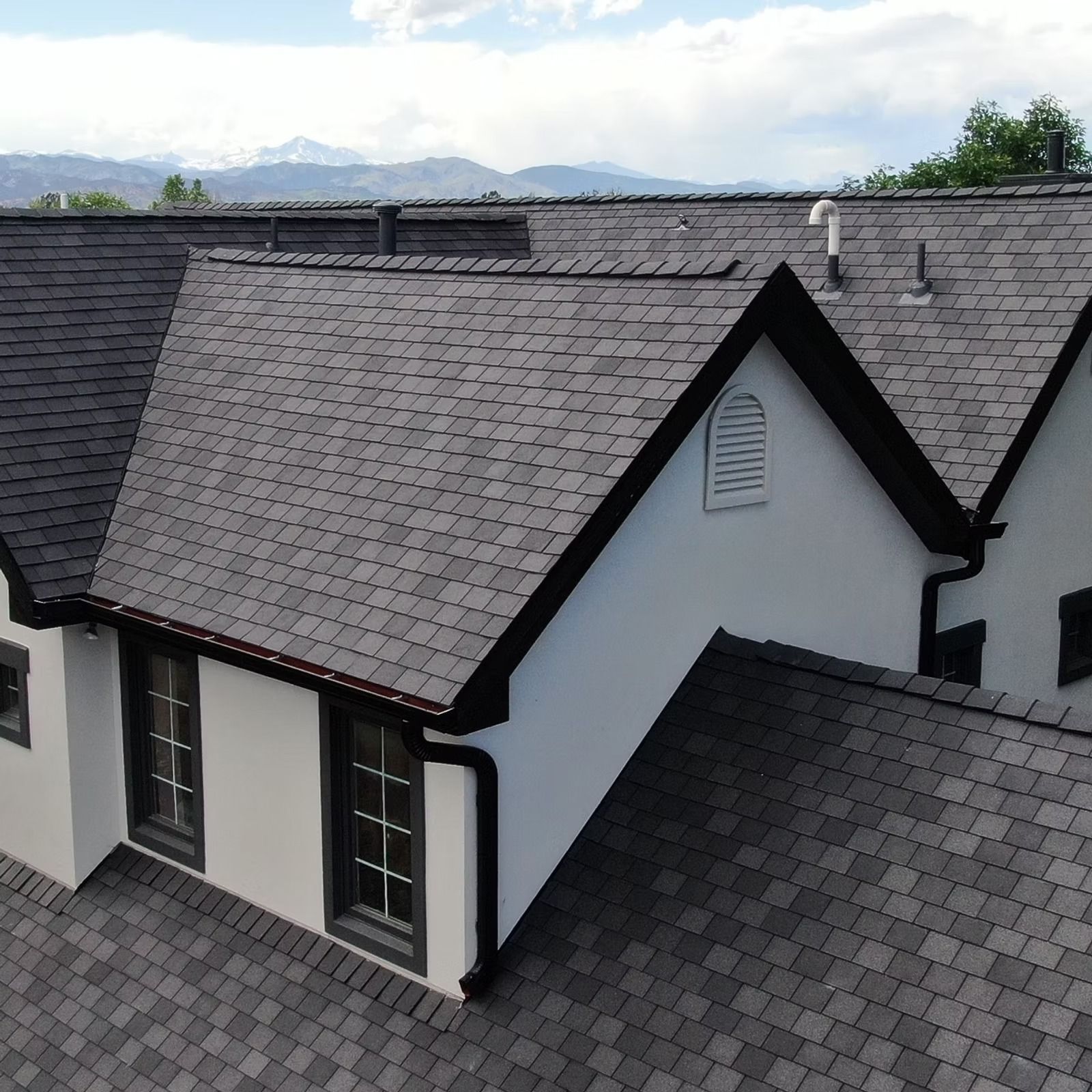 Two adjoining houses with dark gray shingle roofs and white walls, viewed from above.